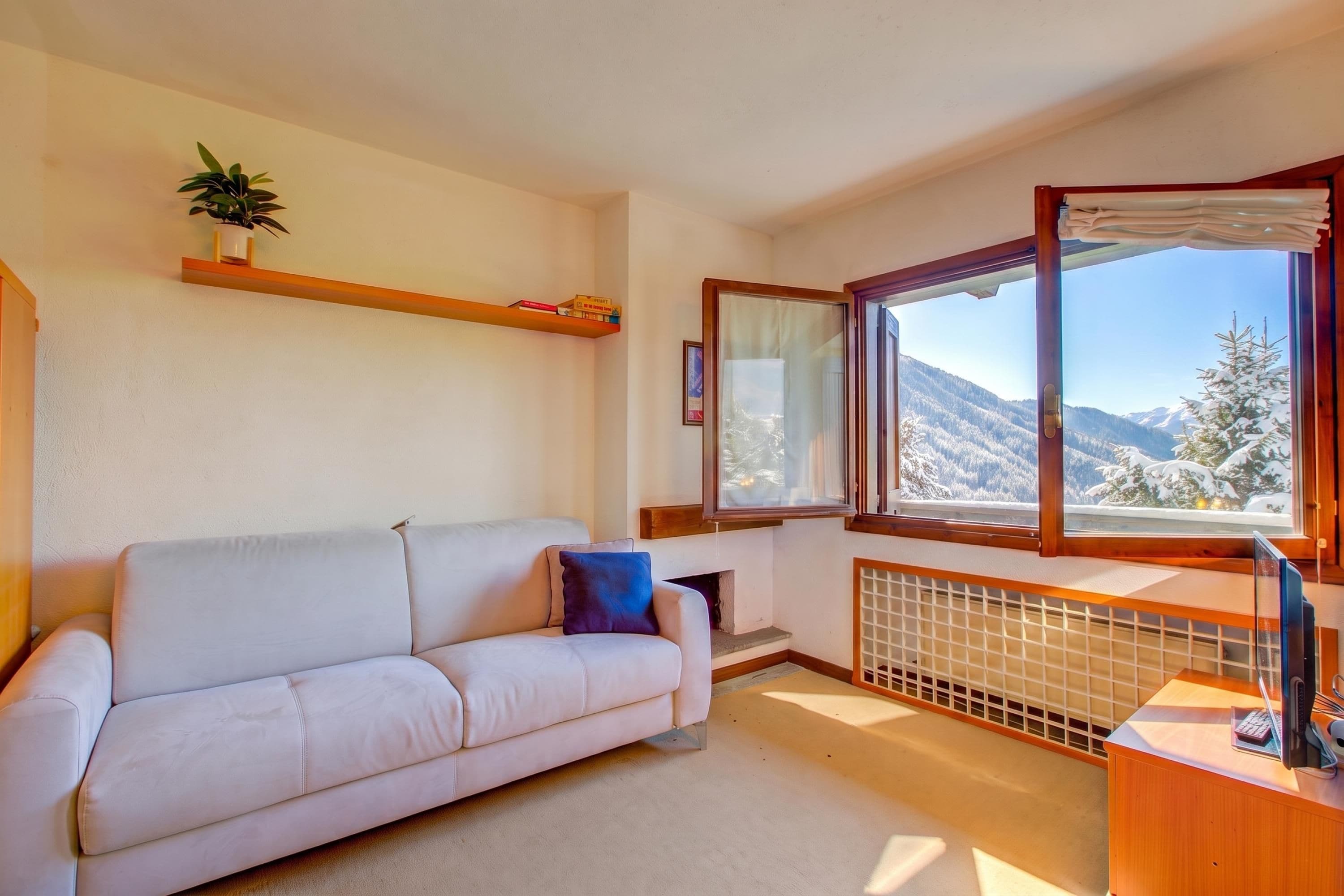 A living room with a sofa, a window with a view of snow-covered mountains, a radiator, and a small table with a keyboard.