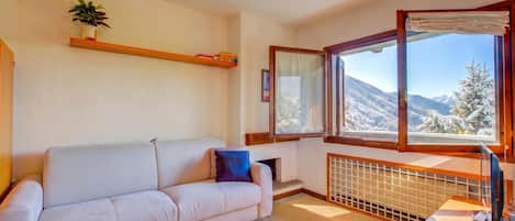 A living room with a sofa, a window with a view of snow-covered mountains, a radiator, and a small table with a keyboard.