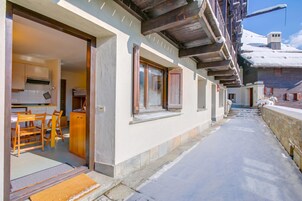 A hotel entrance with a wooden exterior, a visible kitchen area, and a snow-covered path leading to the entrance.