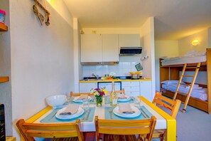 Habitación compacta con una mesa de comedor para dos, kitchenette y una cama litera.