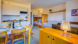 A compact living space with a kitchenette, a dining area, a bunk bed, and a sofa. - Appartamento I Larici (Sauze di Cesana)