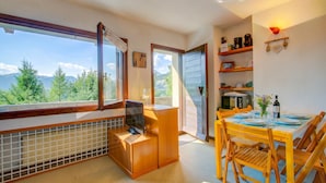 A room with a large window, a dining table set for two, and a kitchen area with a microwave. - Appartamento I Larici (Sauze di Cesana)