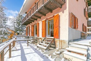 Un edificio con balcón, escalones de madera y alrededores cubiertos de nieve.