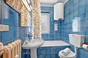 Casa de banho com azulejos azuis, uma pia branca, uma banheira e uma sanita.