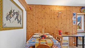 A dining area with a wooden wall, a table set for four, and a window with a view of mountains. - Appartamento La Radura (Claviere)