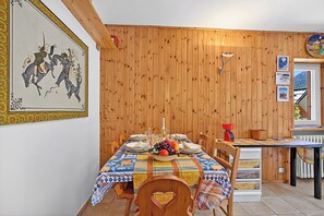 Un comedor con pared de madera, una mesa dispuesta para cuatro personas y un ventanal con vista a las montañas.