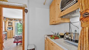 A compact kitchen with wooden cabinets, a built-in stove, and a window overlooking a garden. - Appartamento La Radura (Claviere)