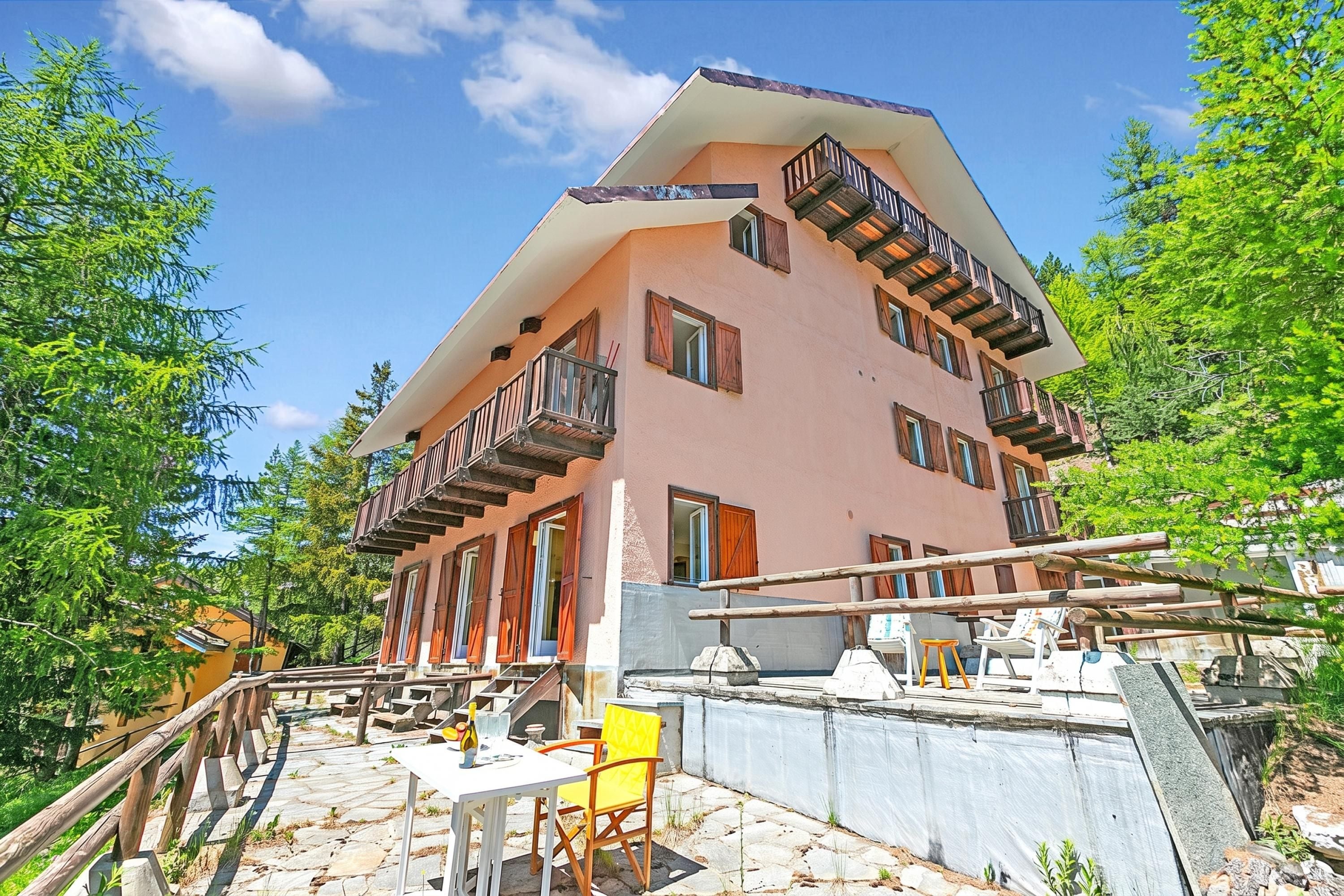 Un immeuble à plusieurs étages doté de balcons, d’une terrasse en pierre et d’un espace extérieur aménagé avec des sièges.