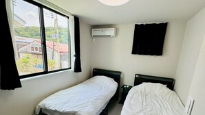 Une chambre d’hôtel avec deux lits simples, une fenêtre avec des rideaux, un appareil de climatisation et une vue sur un bâtiment à l’extérieur.