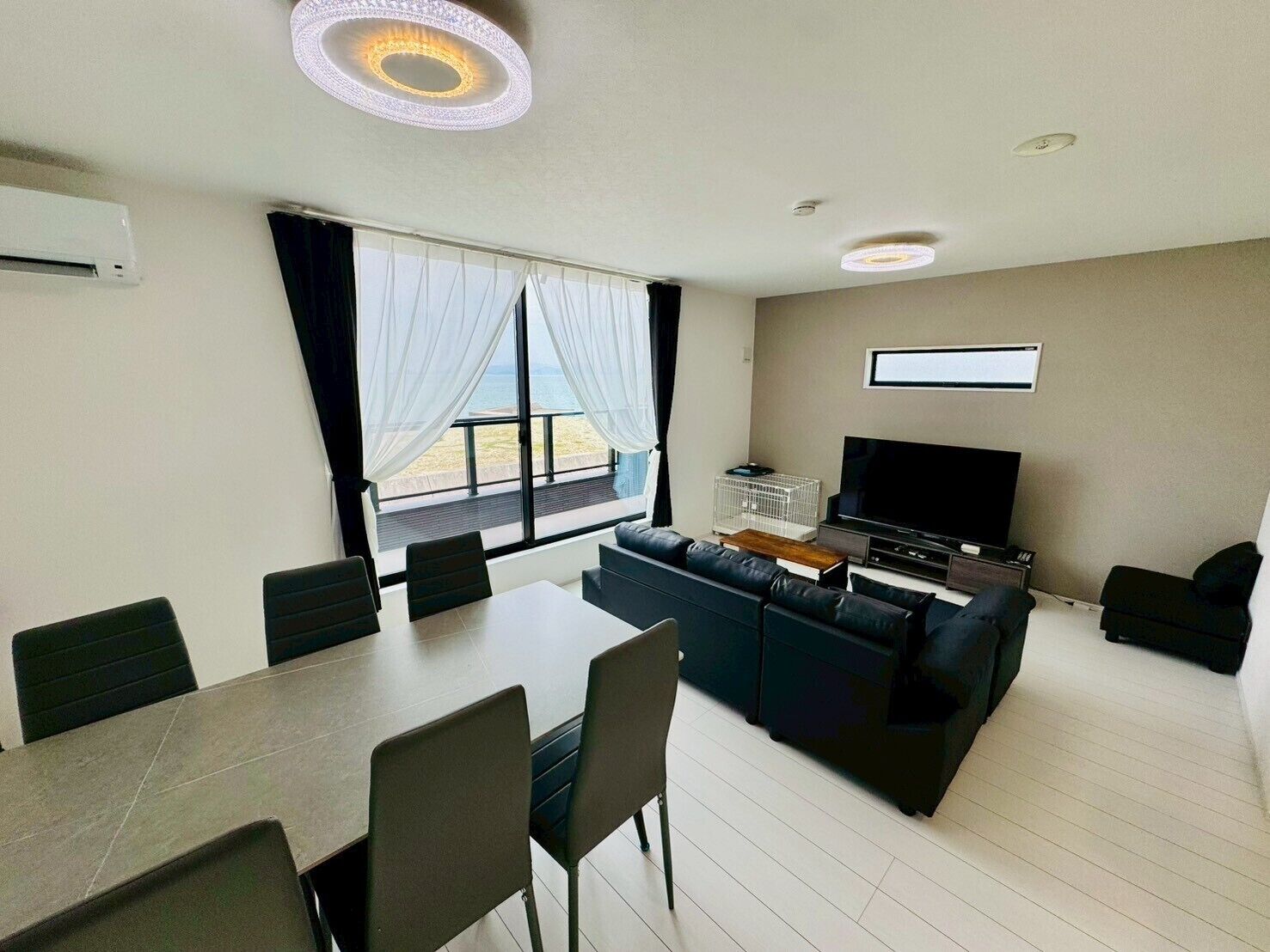 Un salon moderne doté d’un grand téléviseur, d’un canapé, d’une table à manger avec des chaises et offrant une vue sur l’extérieur grâce à une grande fenêtre.