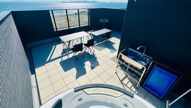 A rooftop terrace with a hot tub, a table, and chairs, overlooking a body of water.