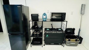 A kitchenette with a refrigerator, microwave, coffee maker, and a small shelf with a kettle and glasses.