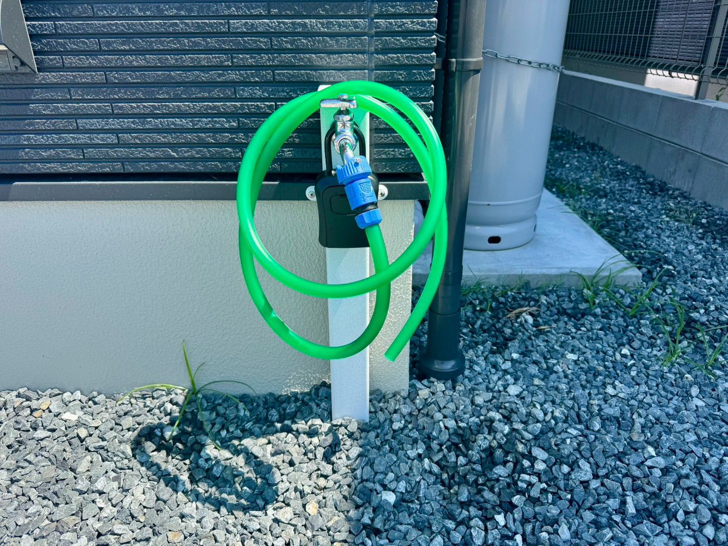 A green garden hose coiled on a concrete post next to a building with a textured facade.