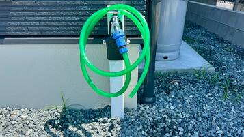 A green garden hose coiled on a concrete post next to a building with a textured facade.