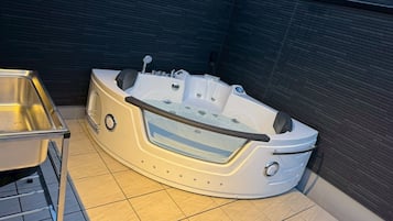 A hot tub with a built-in seat and controls, a metal sink, and a tiled floor.