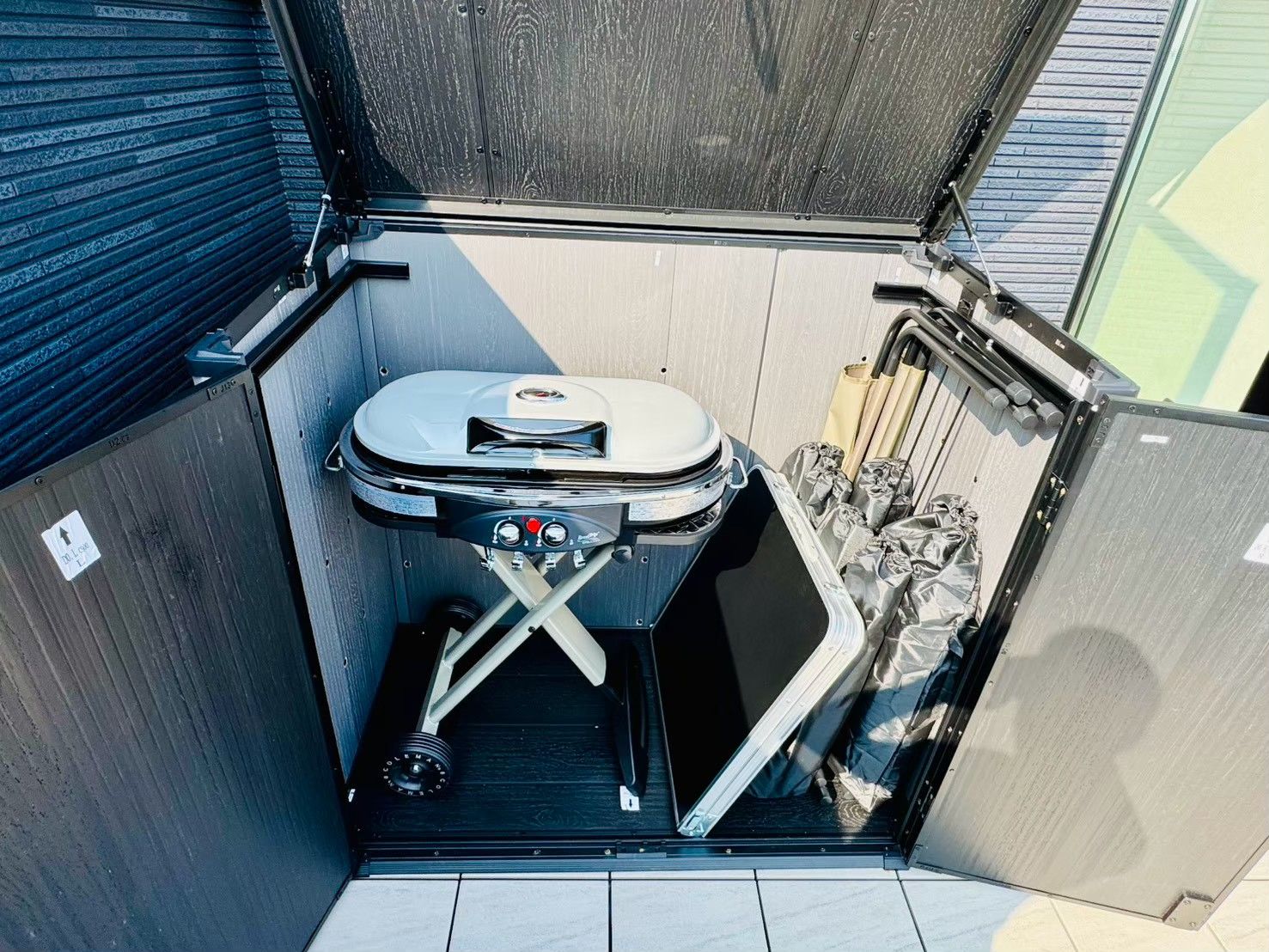 A compact outdoor cooking area with a portable grill, a folding table, and a storage bin with utensils.