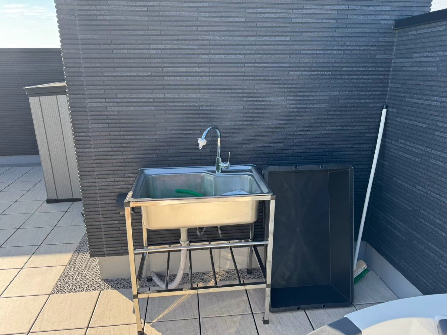 A modern outdoor bathroom with a sink, a shower enclosure, and a broom.