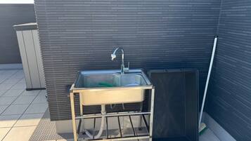 A modern outdoor bathroom with a sink, a shower enclosure, and a broom.