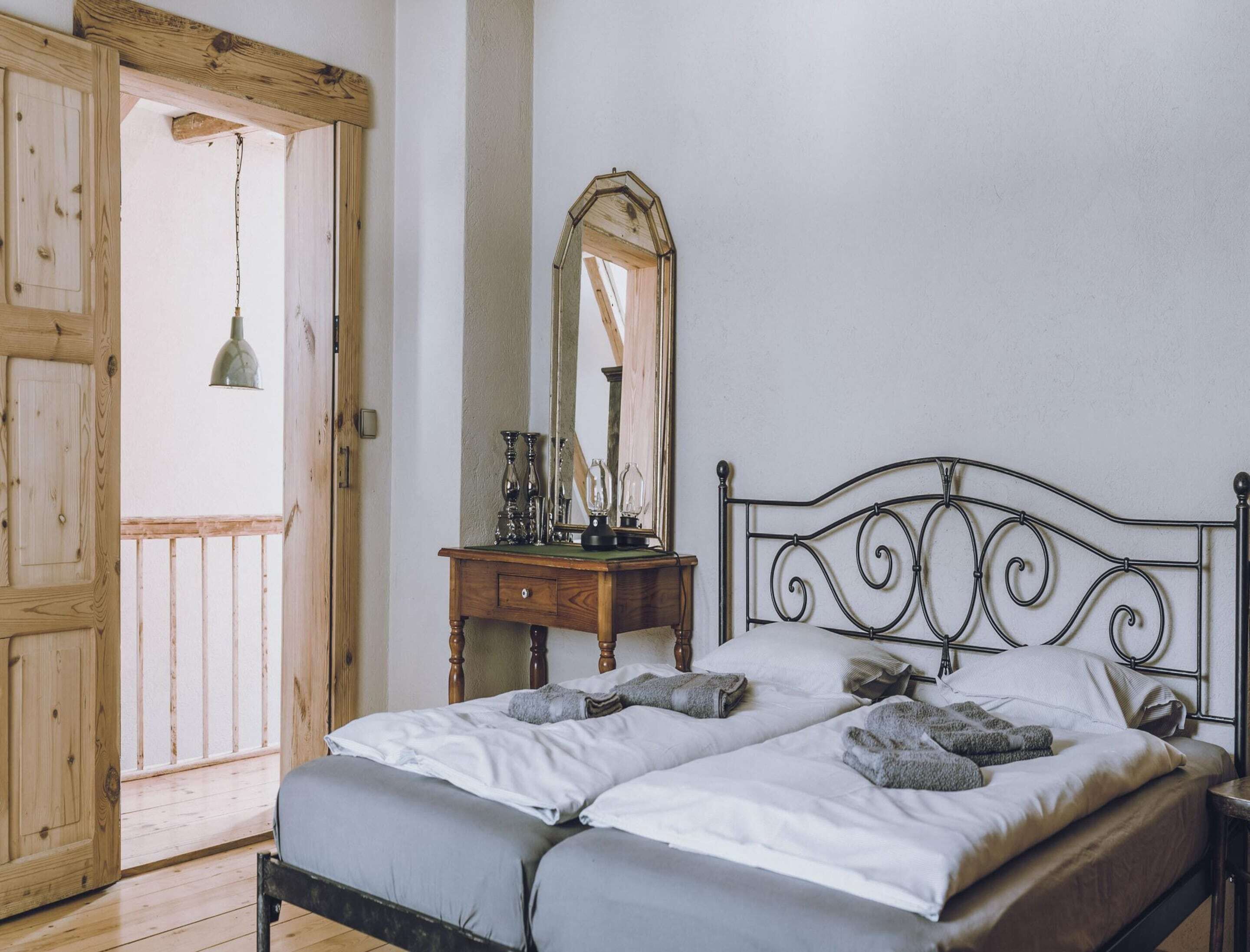 Un dormitorio con puerta de madera, cómoda, espejo y cama con almohadas y manta.