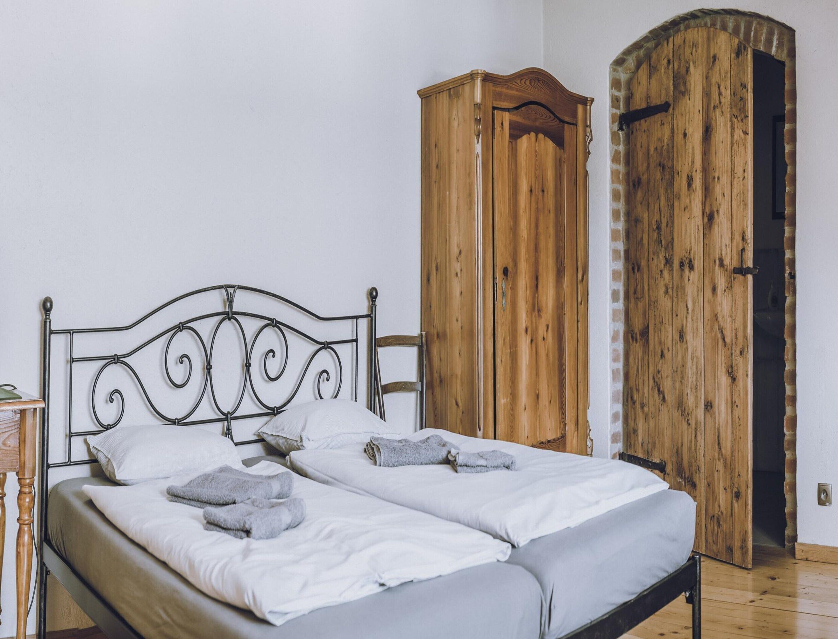 A bed with a metal frame and white bedding, a wooden wardrobe, and a wooden door.