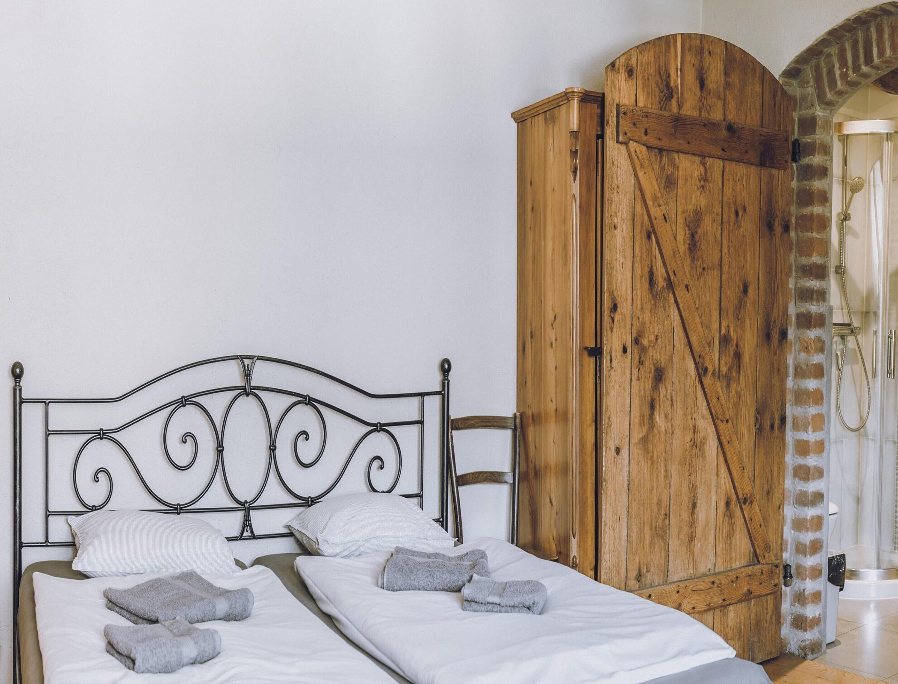 Una cama con cabecera de metal, ropa de cama blanca y dos toallas. Un armario de madera se encuentra a la derecha.