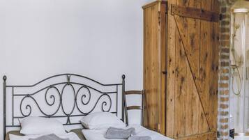 Una cama con cabecera de metal, ropa de cama blanca y dos toallas. Un armario de madera se encuentra a la derecha.