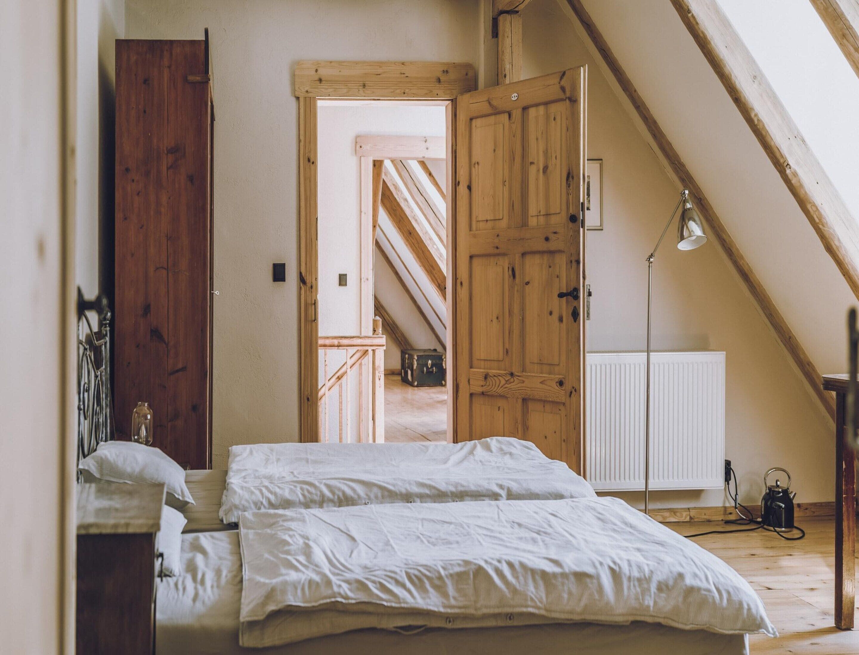 A bedroom with a wooden door, a radiator, and a bed with white bedding.
