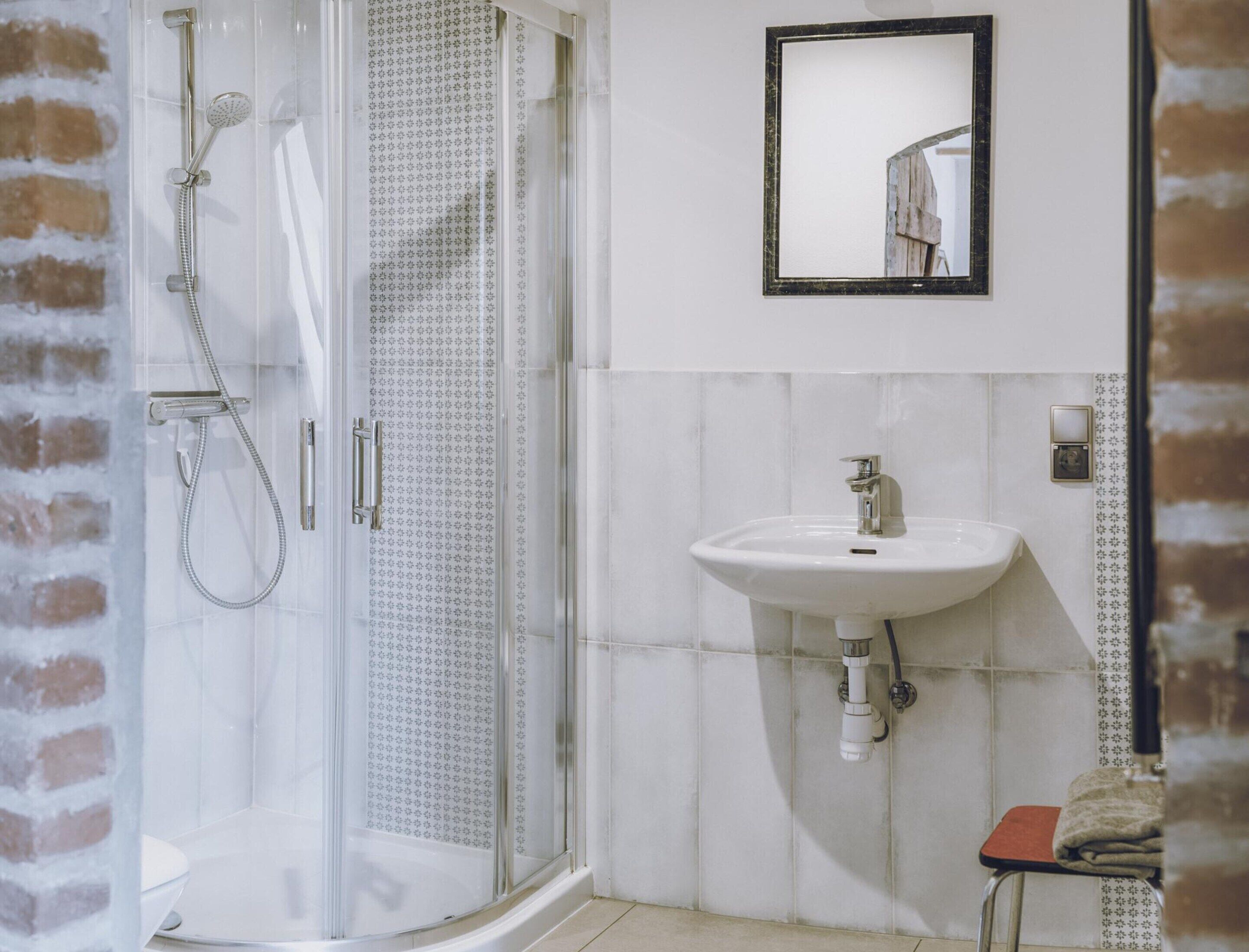 Un baño con cabina de ducha de vidrio, un lavabo blanco y un espejo en la pared.