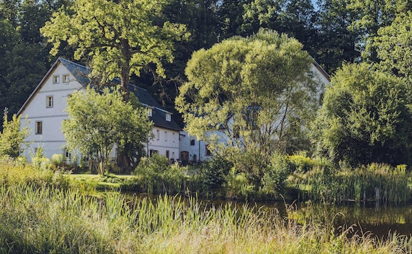 A white building with multiple windows, surrounded by lush greenery and a body of water. - Country Stay for Two Guests (Janowice Wielkie)