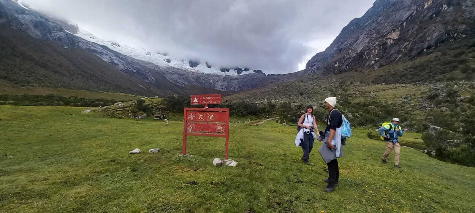 Un paisaje montañoso con un cartel rojo y excursionistas.