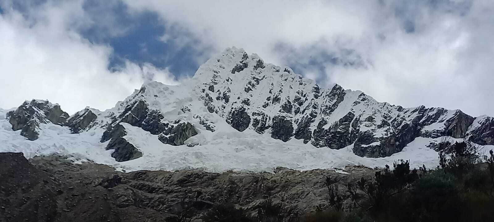 A snow-covered mountain range with rocky outcrops and sparse vegetation at the base.