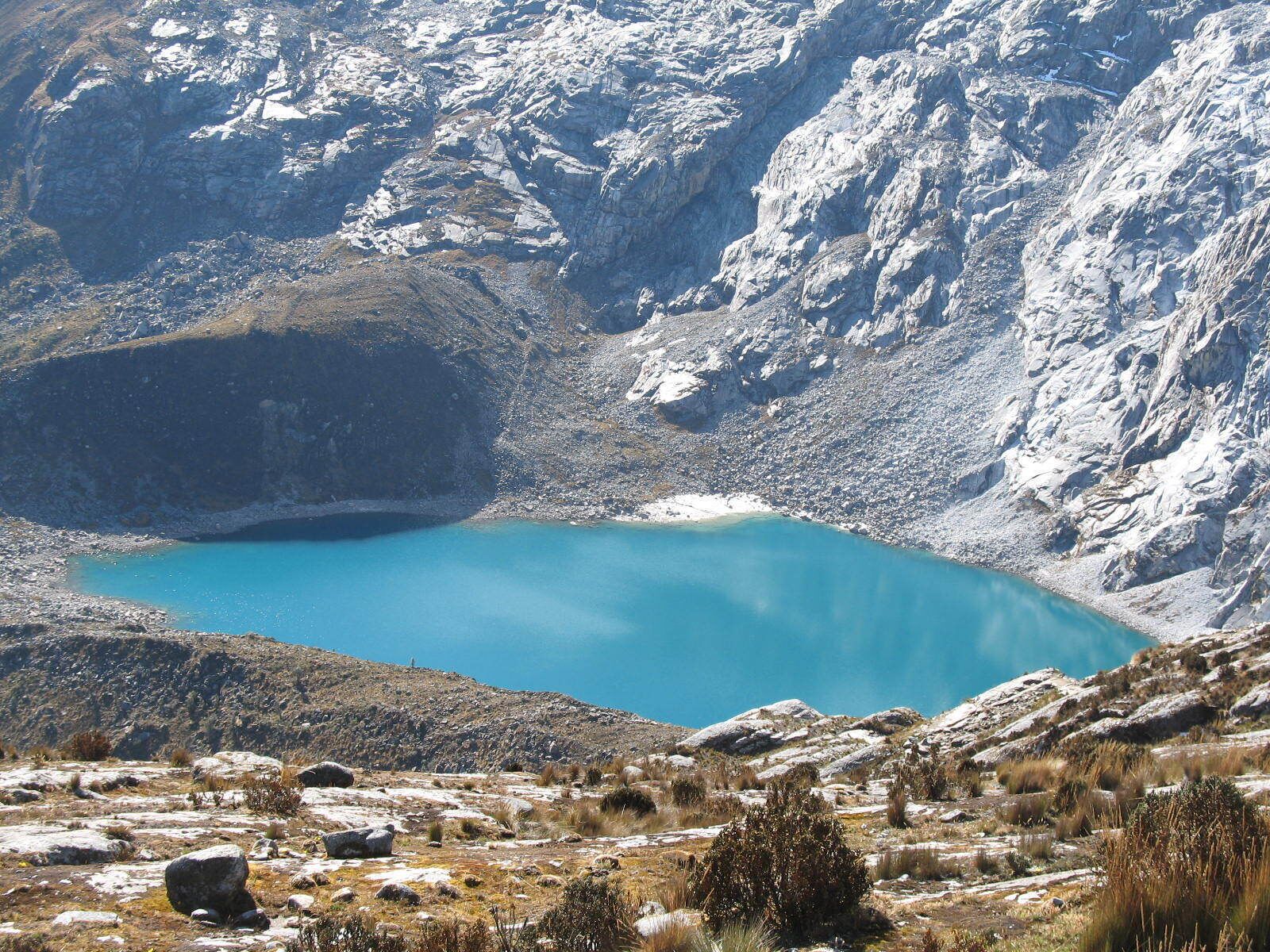 A mountainous landscape with a clear blue lake surrounded by rocky terrain and sparse vegetation.