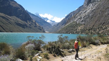 A hiker on a rocky trail with a mountainous backdrop and a lake.