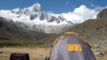 A tent in a mountainous area with a snow-capped peak in the background.