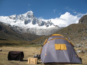 Una tienda de campaña en una zona montañosa con un pico nevado al fondo.