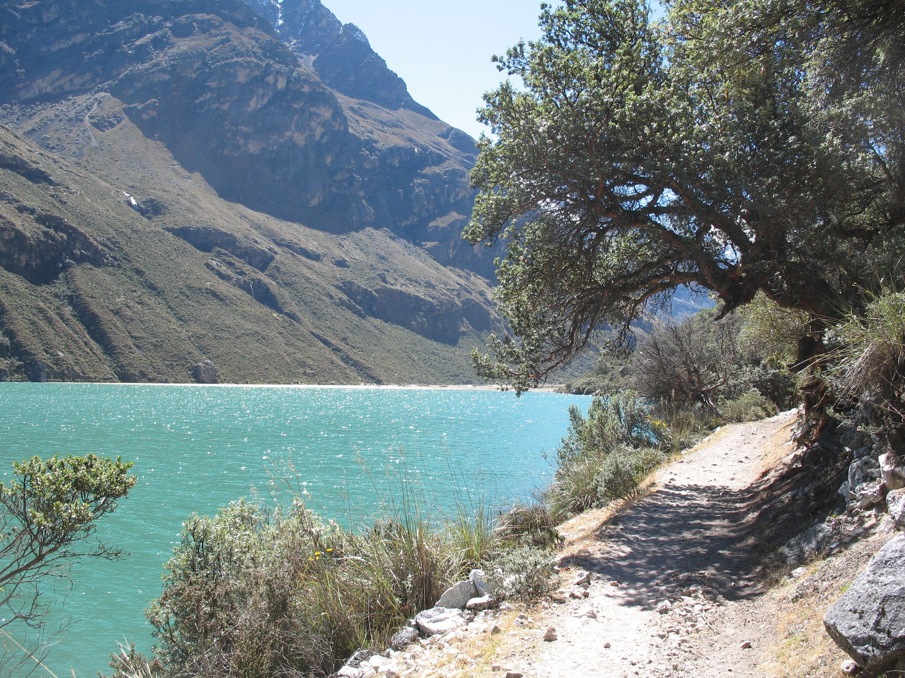 A mountainous landscape with a clear turquoise lake, a dirt path, and sparse vegetation.
