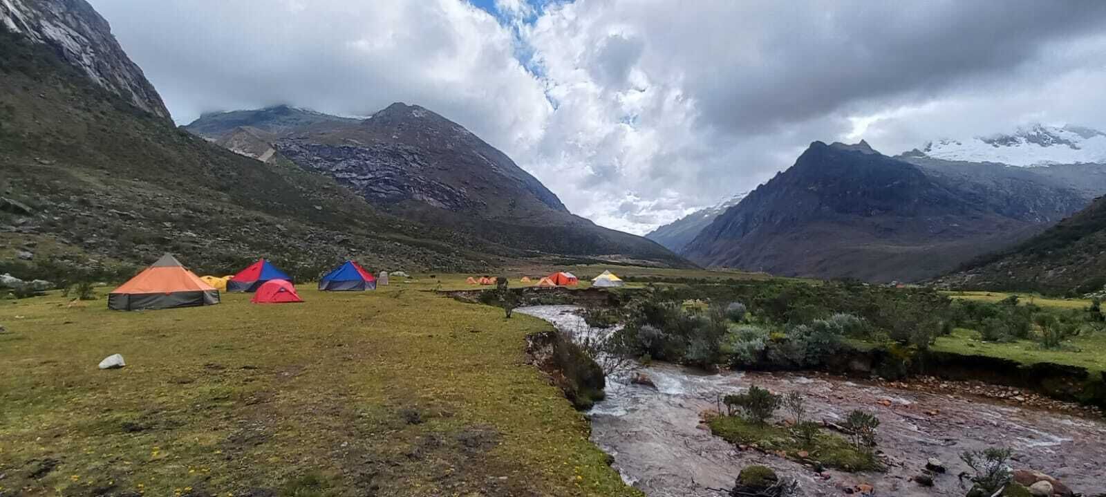 Un paisaje montañoso con varias tiendas de campaña instaladas en un campo cubierto de hierba.