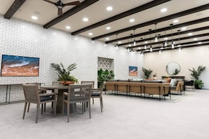 Un comedor moderno con pared de ladrillo, ventilador de techo, iluminación colgante y un cuadro grande.