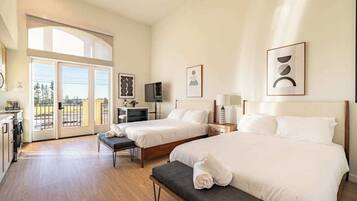 A hotel room with two beds, a desk, a TV, and a balcony with a view.