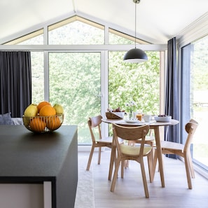 A modern dining area with a table set for breakfast, large windows, and a view of greenery.