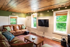 A cozy living room with a leather sofa, a wooden coffee table, and a flat-screen TV mounted on the wall. - Red Farmhouse By The Creek (Scott Township)