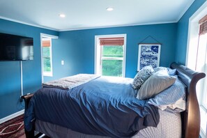 A bedroom with a bed, a TV, and a window with a view of greenery. - Red Farmhouse By The Creek (Scott Township)