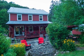 A two-story house with a porch, outdoor seating, and a stone feature. - Red Farmhouse By The Creek (Scott Township)