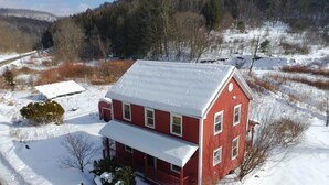 Ett rött hus i två våningar med ett snötäckt tak, omgivet av ett snöigt landskap och en skogbeklädd kulle i bakgrunden.