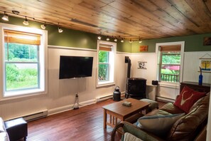 A cozy living room with a wooden ceiling, a flat-screen TV mounted on the wall, a fireplace, and a comfortable couch. - Red Farmhouse By The Creek (Scott Township)