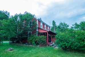 A red wooden house with a porch, surrounded by lush greenery and trees. - Red Farmhouse By The Creek (Scott Township)