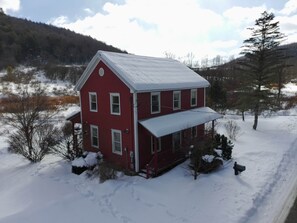 A red two-story house with a covered porch in a snowy landscape. - Red Farmhouse By The Creek (Scott Township)
