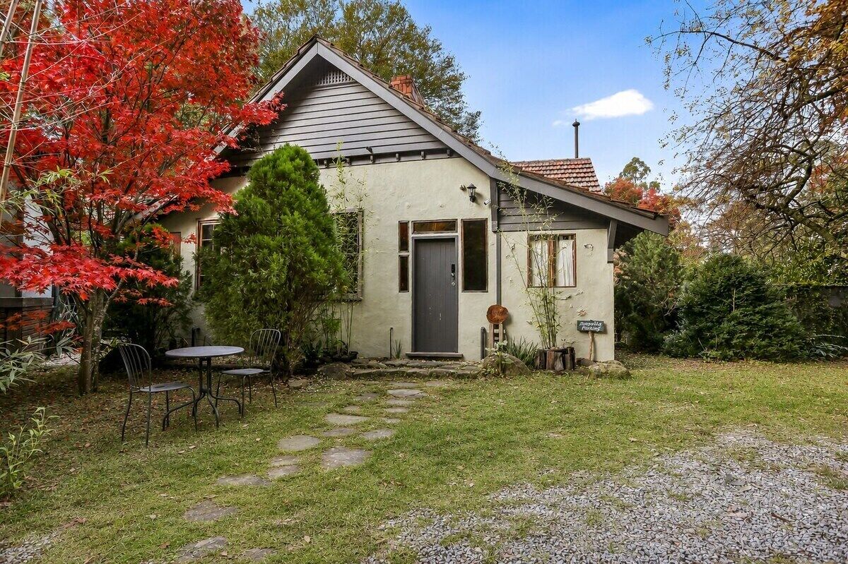 A single-story house with a grey roof, a dark front door, and a small porch with two chairs.