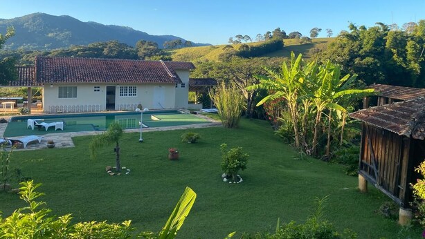 Uma casa com piscina, cercada por vegetação exuberante e colinas ao fundo.