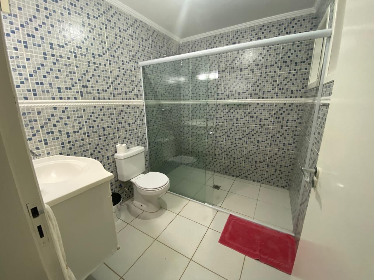 Un baño con ducha envuelta en vidrio, inodoro y lavamanos.